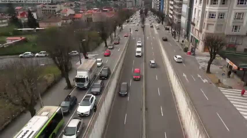 A high-angle view shows a multi-lane road with moderate traffic on an overcast day, flanked by buildings and trees.