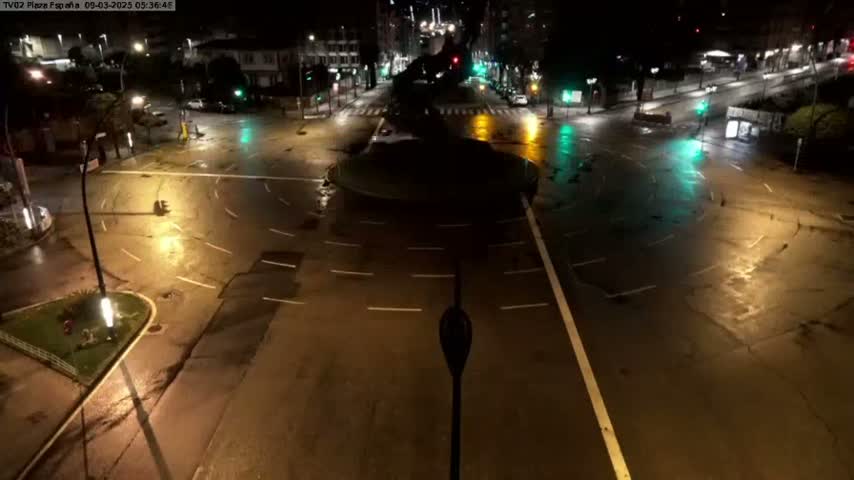 A wet, empty roundabout and surrounding streets are illuminated at night by streetlights.