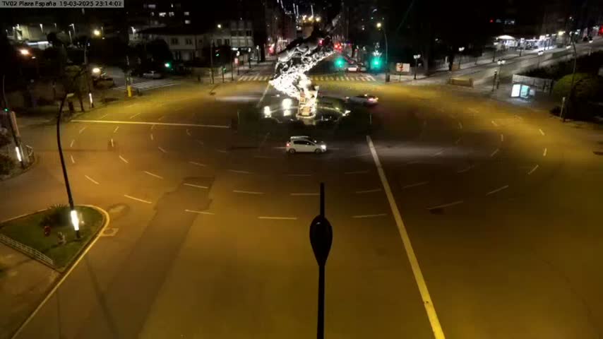 A nighttime aerial view of a roundabout with a few cars, illuminated by streetlights.