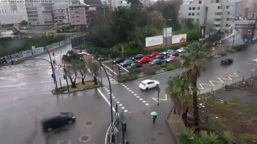 A rainy day scene shows a busy intersection with cars and a pedestrian, surrounded by buildings and trees.