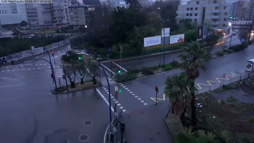 A wet, rainy city intersection shows a pedestrian crossing, traffic lights, and buildings in the background.