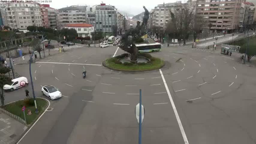 A roundabout in a city with a large sculpture in the center, a few cars, and overcast weather.