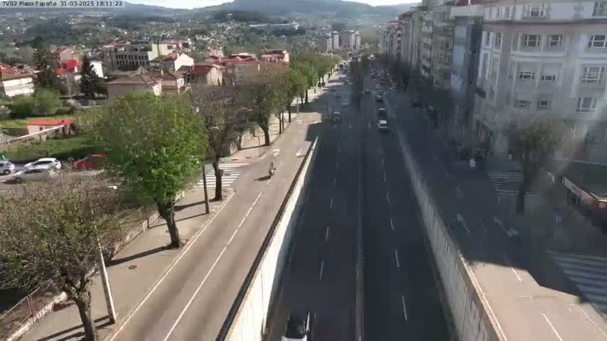 A sunny, high-angle view of a multi-lane road flanked by buildings and trees, with several vehicles traveling in both directions.