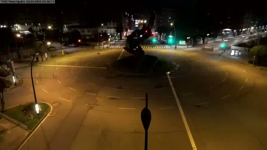 A mostly empty roundabout at night, illuminated by streetlights, with a dark sculpture at its center.