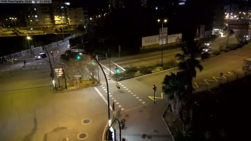 A high-angle nighttime view shows a multi-lane road intersection with sparse traffic, pedestrians, and streetlights illuminating the scene.
