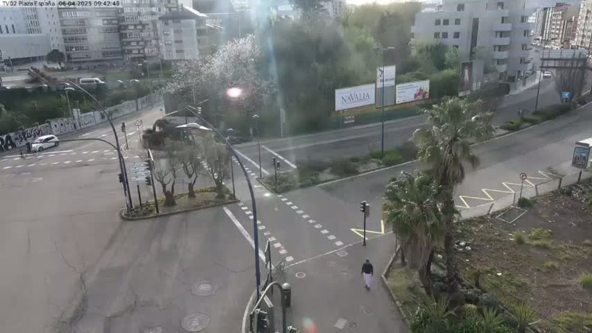 A high-angle view of a city intersection on an overcast day, showing cars, pedestrians, and buildings in the background, with some trees and greenery present.