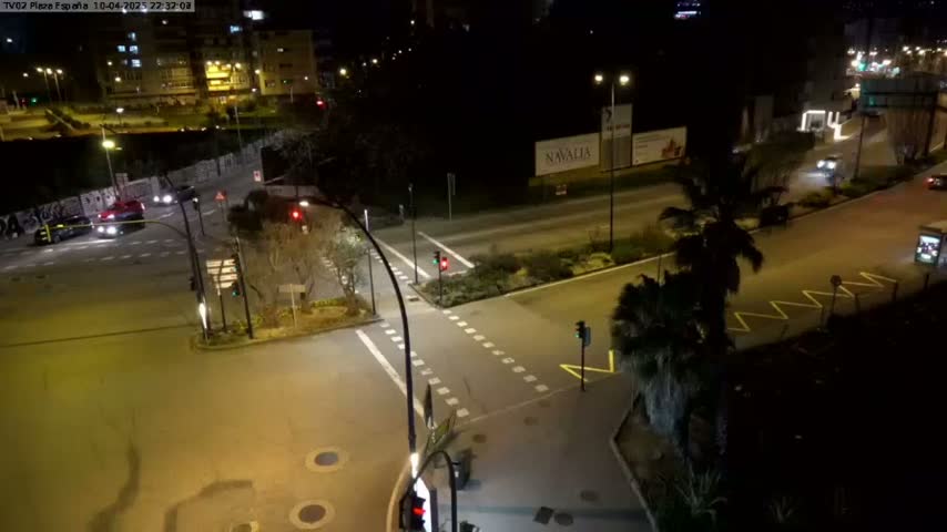 A nighttime, high-angle view of a street intersection with several cars and traffic lights, illuminated by streetlights.