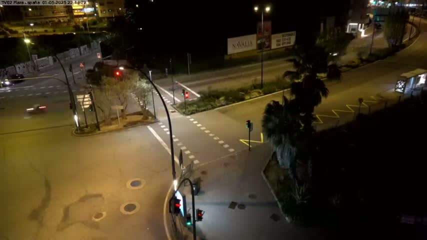 A nighttime, overhead view of a multi-lane road intersection with sparse traffic, streetlights, and palm trees.