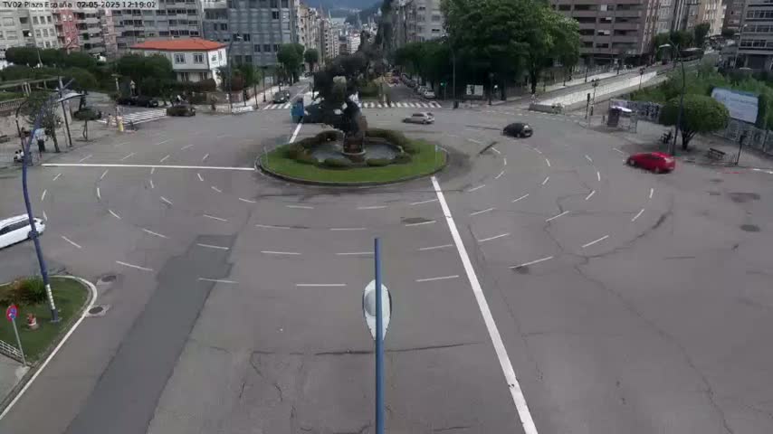 A mostly empty roundabout with a large sculpture in the center is surrounded by buildings and a few cars on a partly cloudy day.