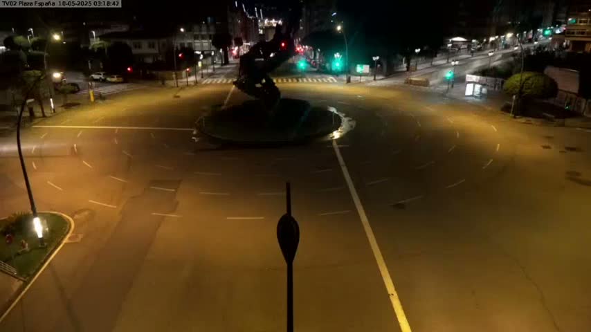 A mostly empty roundabout at night with a dark statue in the center, illuminated by streetlights.