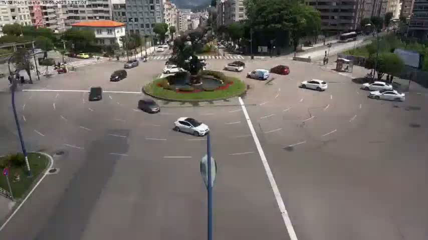 Several cars circulate a roundabout in a city, under a clear sky.