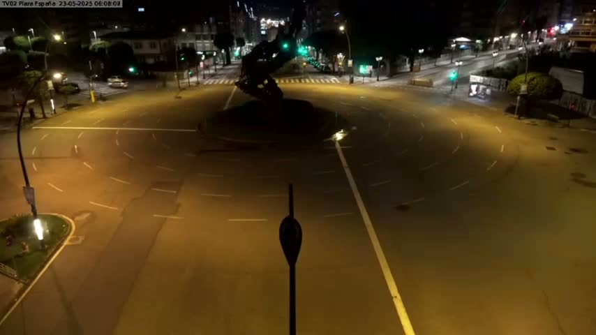 A mostly empty roundabout at night, illuminated by streetlights, with a dark sculpture in the center.