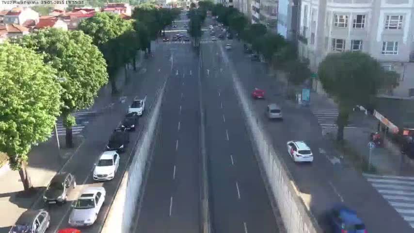 A sunny day view of a multi-lane road with cars driving in both directions, lined with trees and buildings.