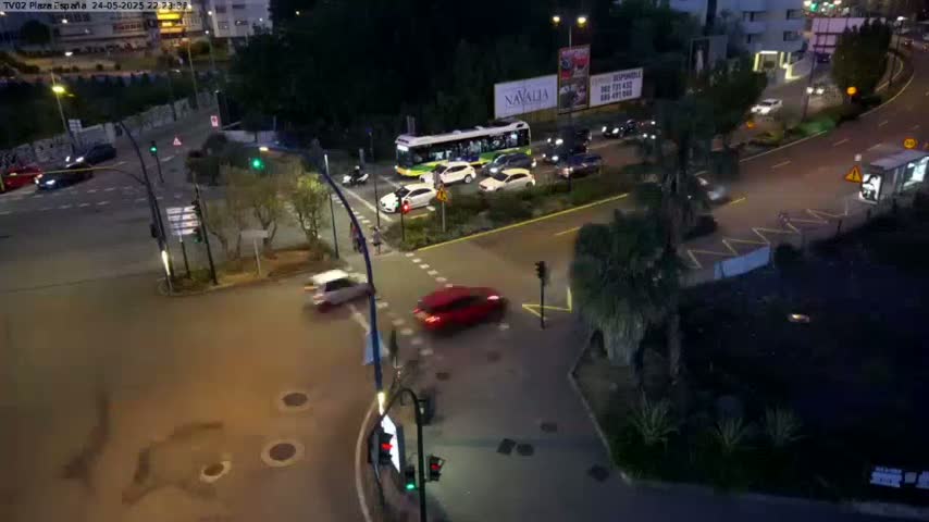 A nighttime aerial view of a busy intersection with several cars and a bus, under partly cloudy skies.