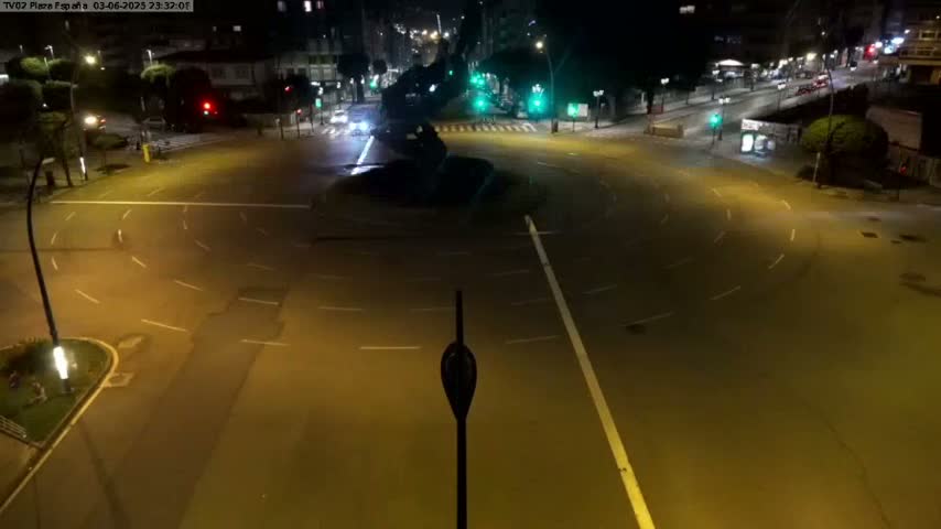 A mostly empty roundabout at night is illuminated by streetlights.