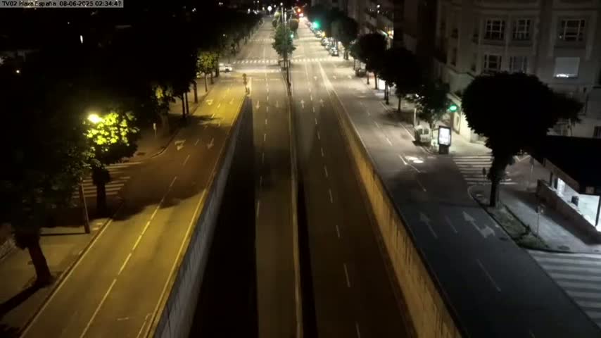 A mostly empty, well-lit city street at night, flanked by buildings and trees.