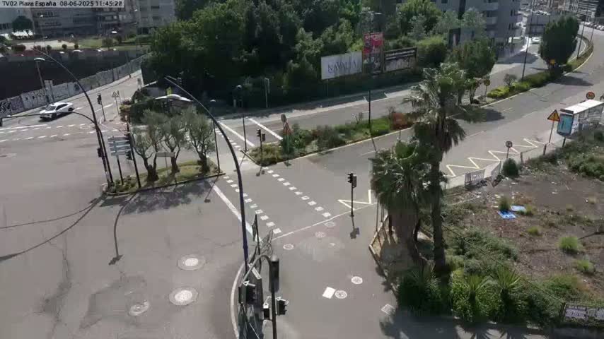 A sunny day shows a high-angle view of a city intersection with traffic lights, palm trees, and a few cars.