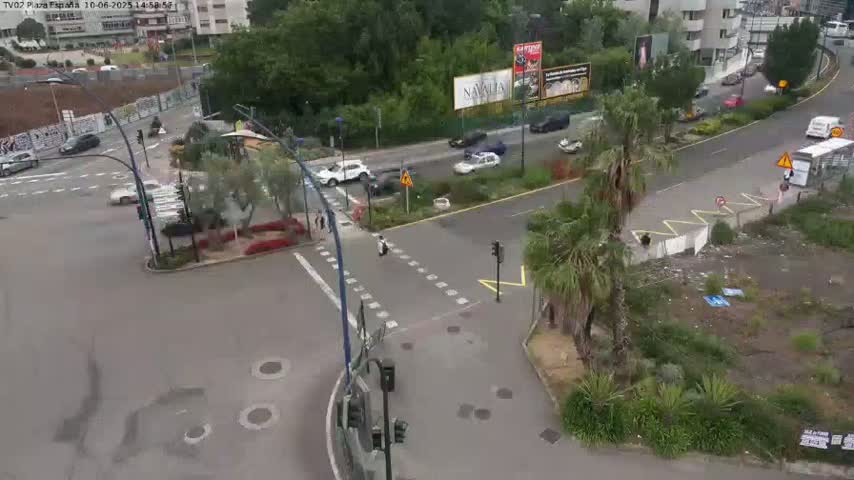 An aerial view shows a city intersection with several cars and a person on a scooter, under a partly sunny sky.