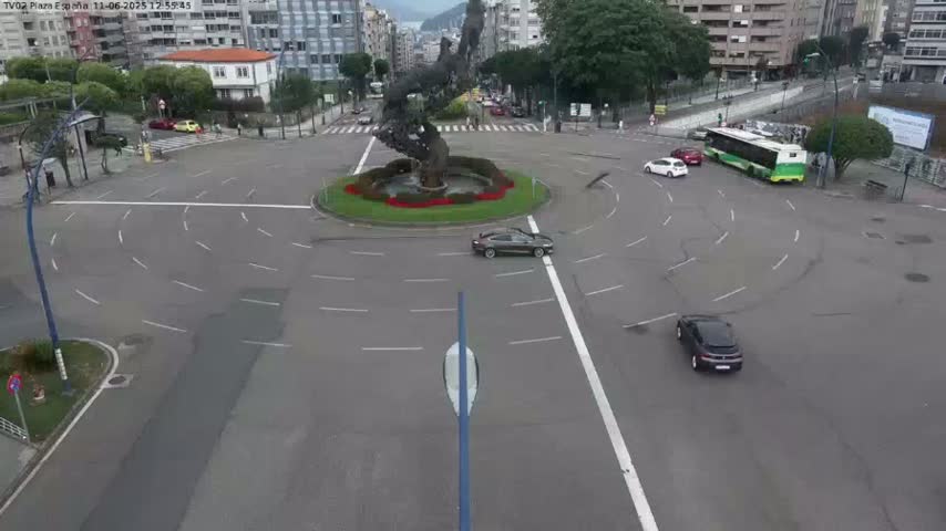 A roundabout with a large sculpture in the center, surrounded by several cars and a bus, on a mostly overcast day.