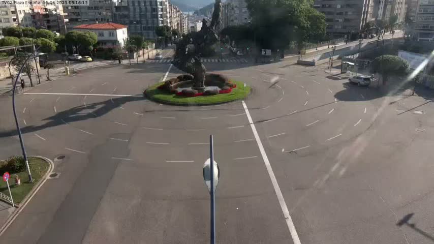 A mostly empty roundabout with a large statue in the center is viewed from above on a sunny day.