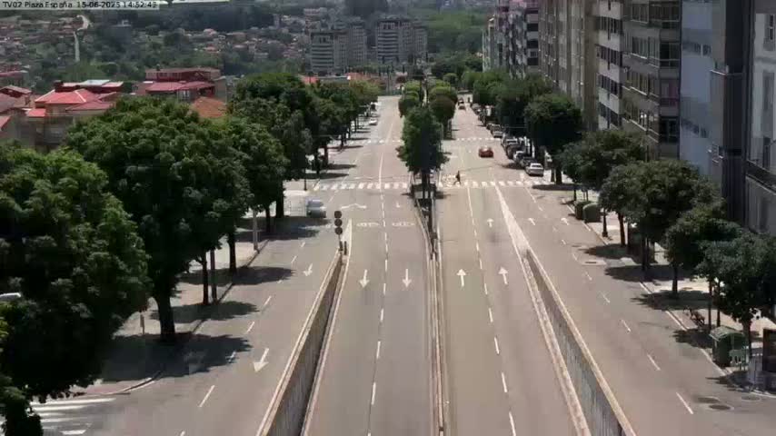 A mostly empty, wide, multi-lane road lined with trees and buildings on a sunny day.