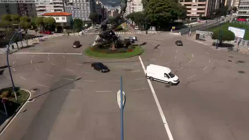 A sunny day shows numerous cars driving in both directions down a tree-lined city street.