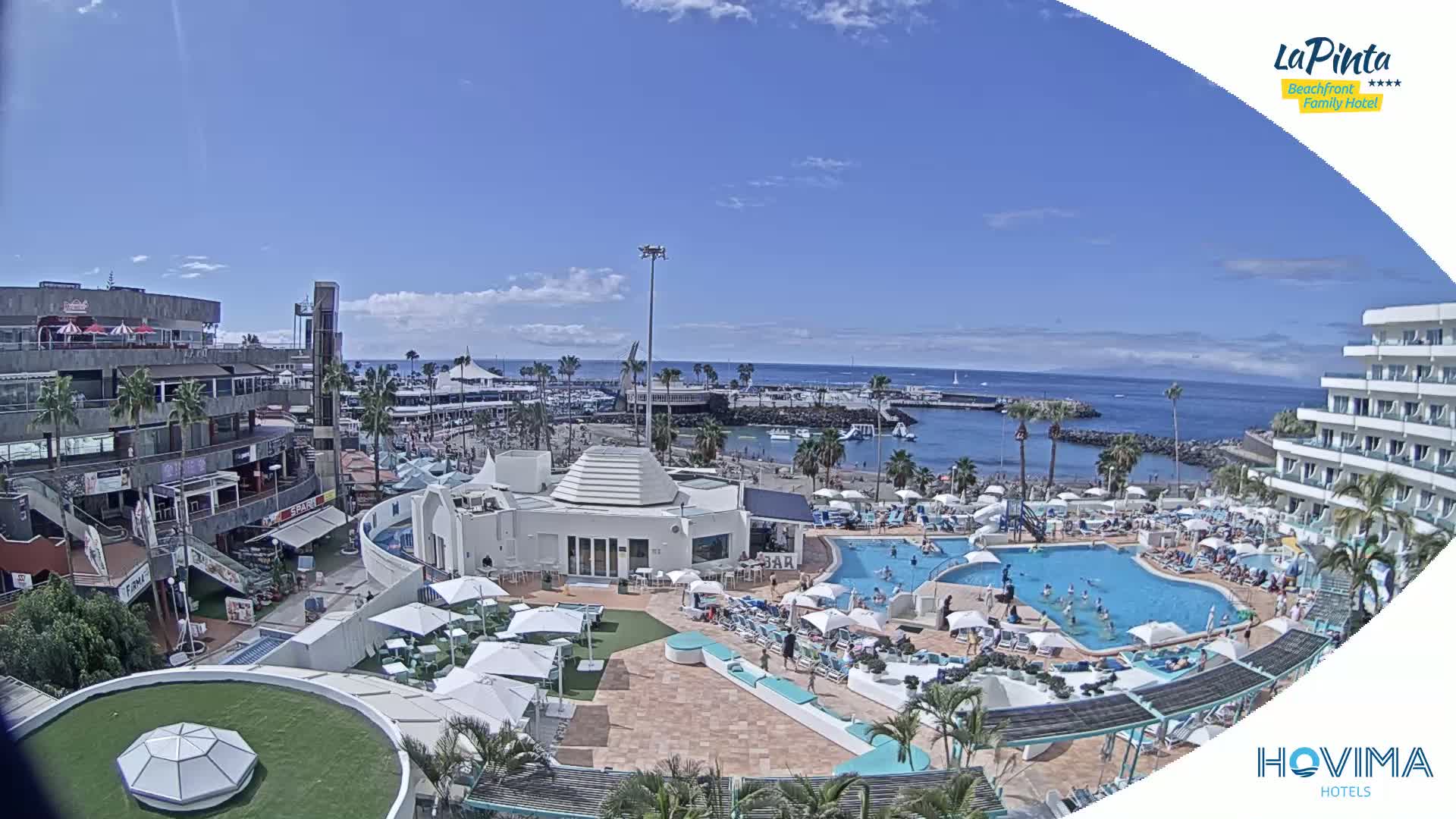 A sunny day overlooking a resort pool area, beach, and harbor with clear blue water.