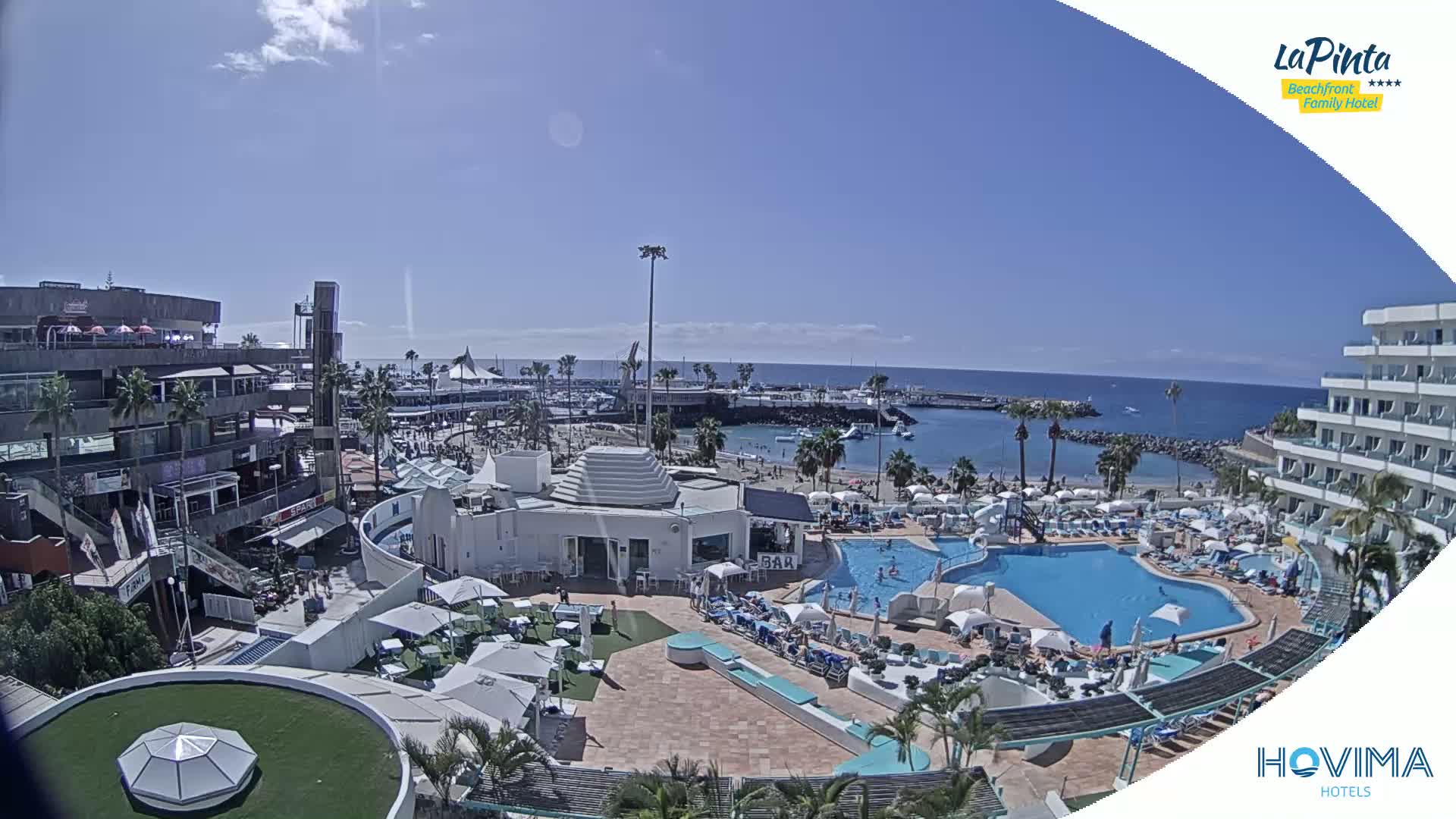 A resort pool area with a beach and calm ocean in the background under sunny skies.