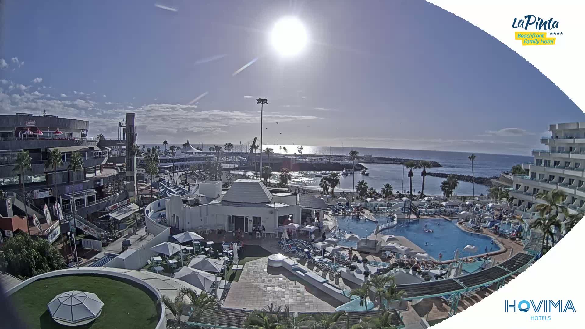 A sunny day overlooking a resort with a swimming pool, beach, and harbor, showcasing a bright, clear sky.
