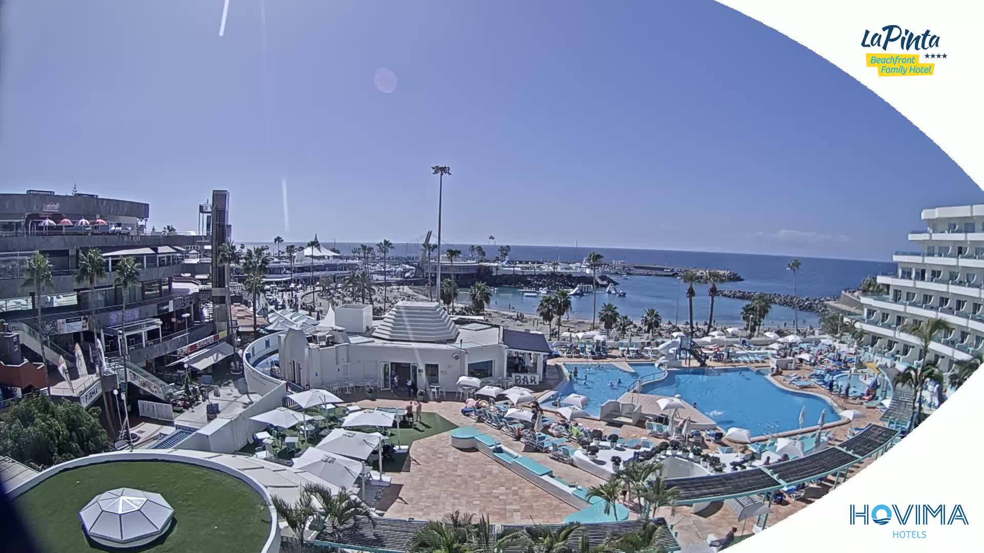 A sunny day overlooking a resort with a pool and beach, next to a calm ocean.