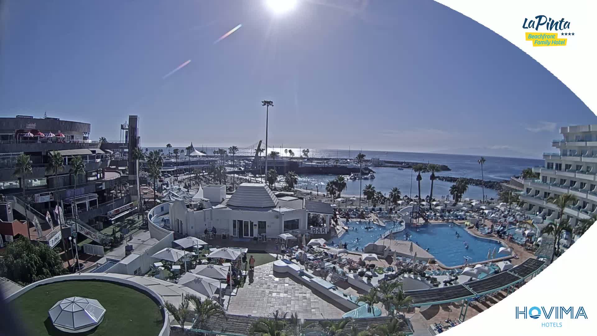 A sunny day overlooking a resort with a swimming pool and beach area adjacent to a marina and ocean.