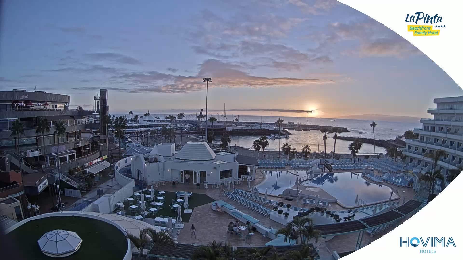 A resort pool area and marina are seen at sunset under a mostly clear sky.