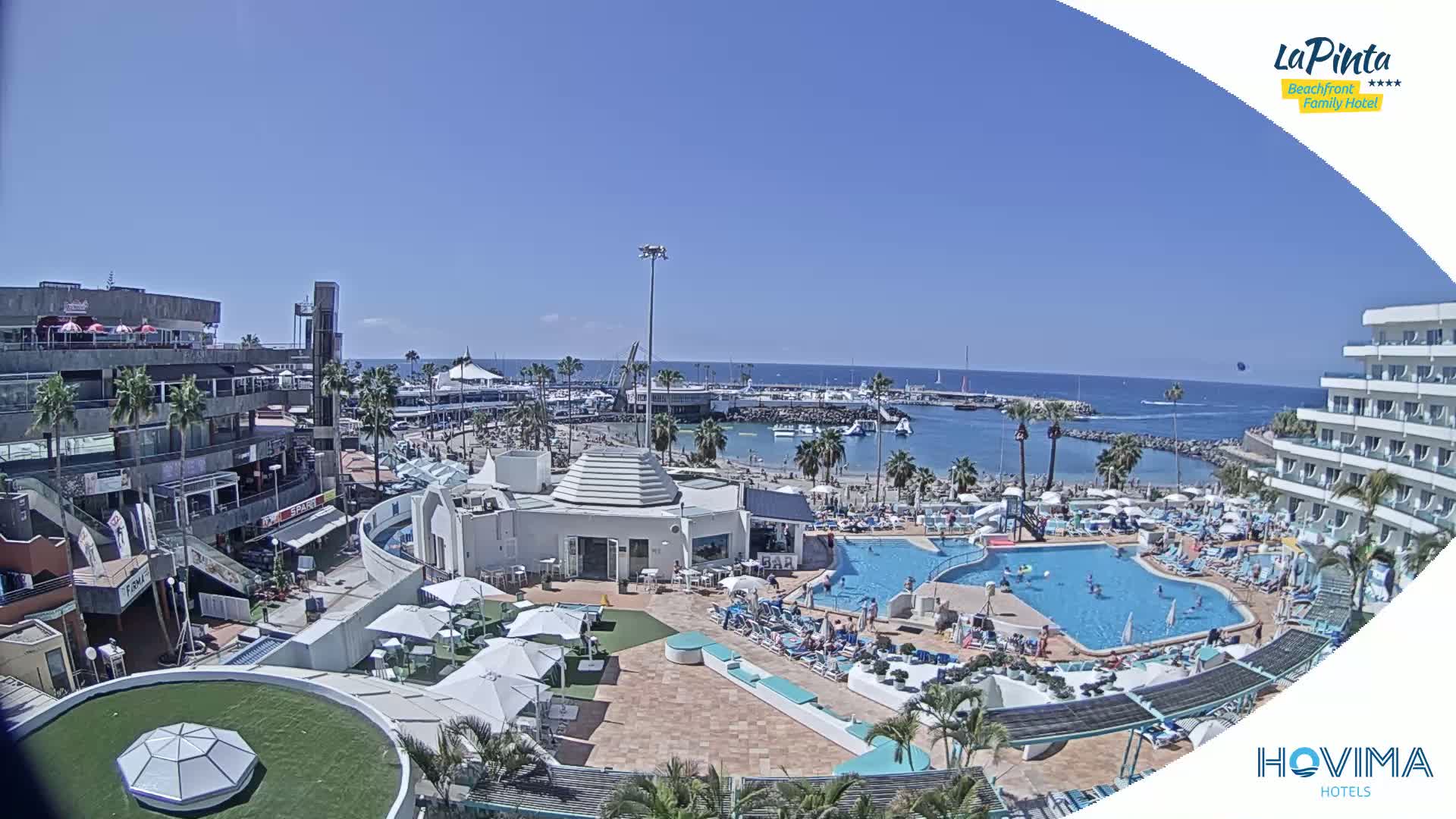 A sunny day overlooking a resort with multiple pools, a beach, a marina, and buildings.