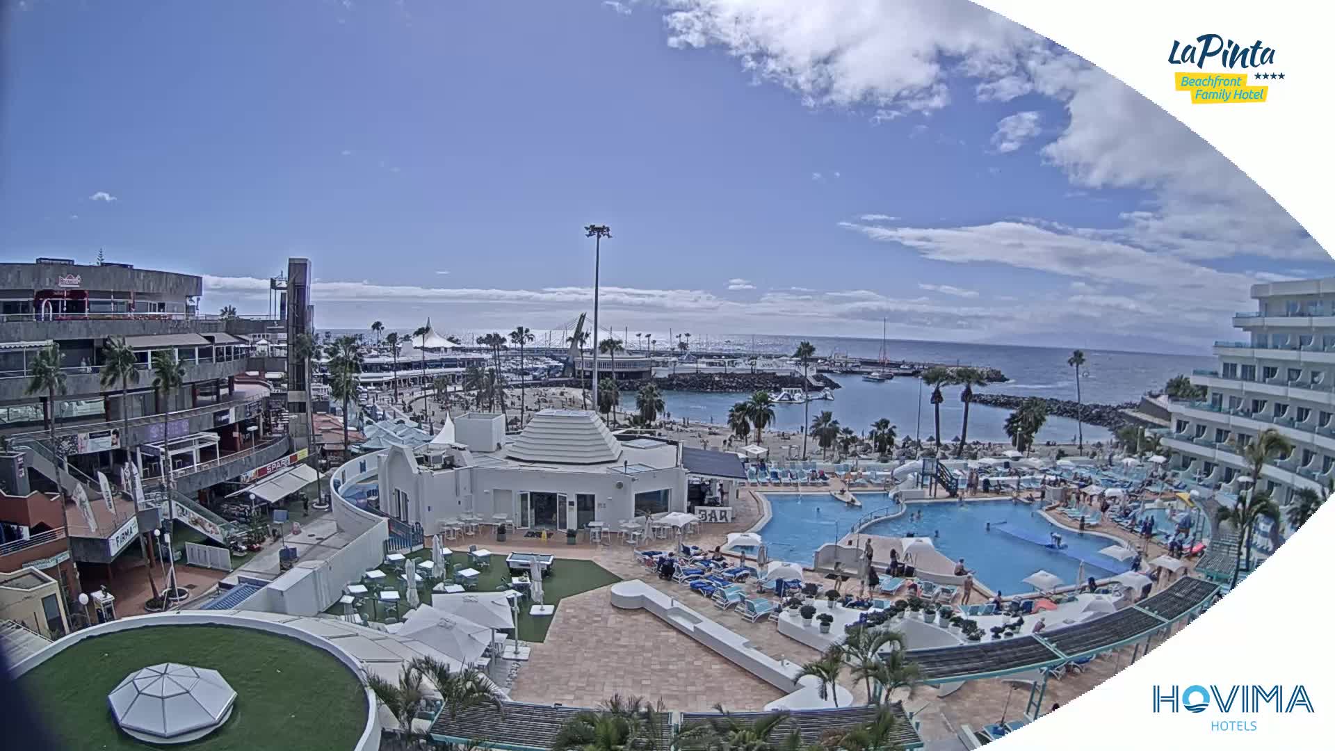 A sunny day overlooking a resort with a pool, beach, marina, and shops.