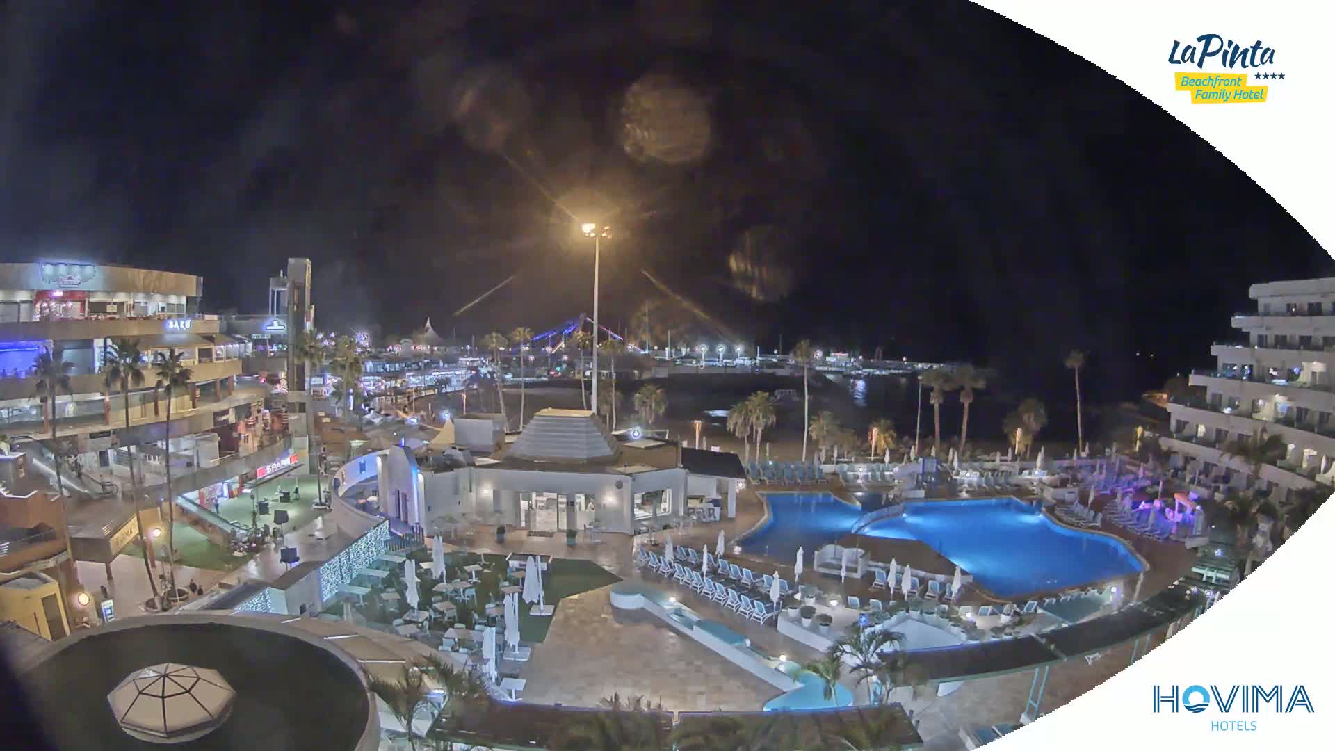 A nighttime view of a resort complex with swimming pools and surrounding buildings, lit up against a dark sky.