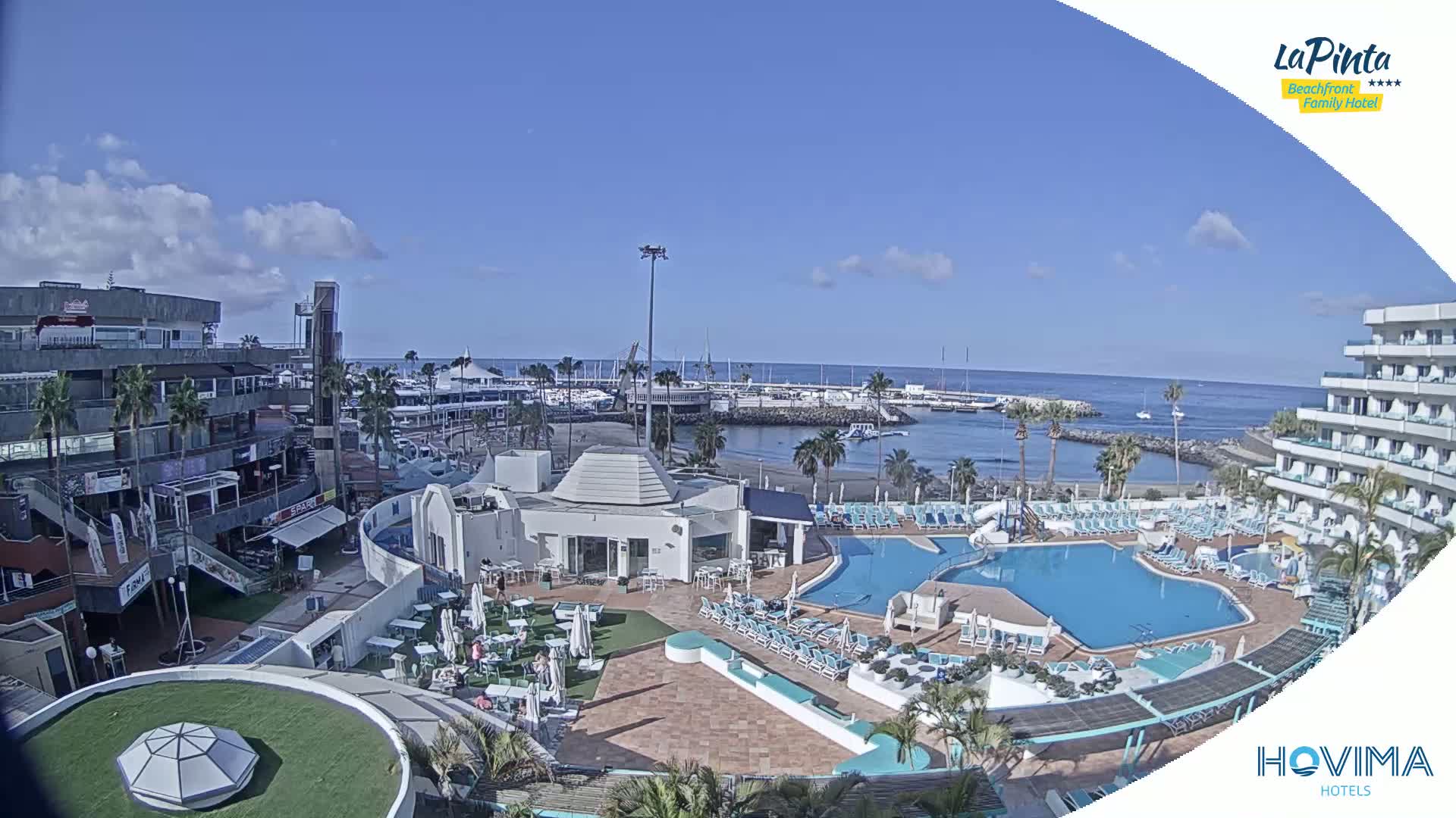 A resort pool area with a marina and ocean in the background under a mostly sunny sky.