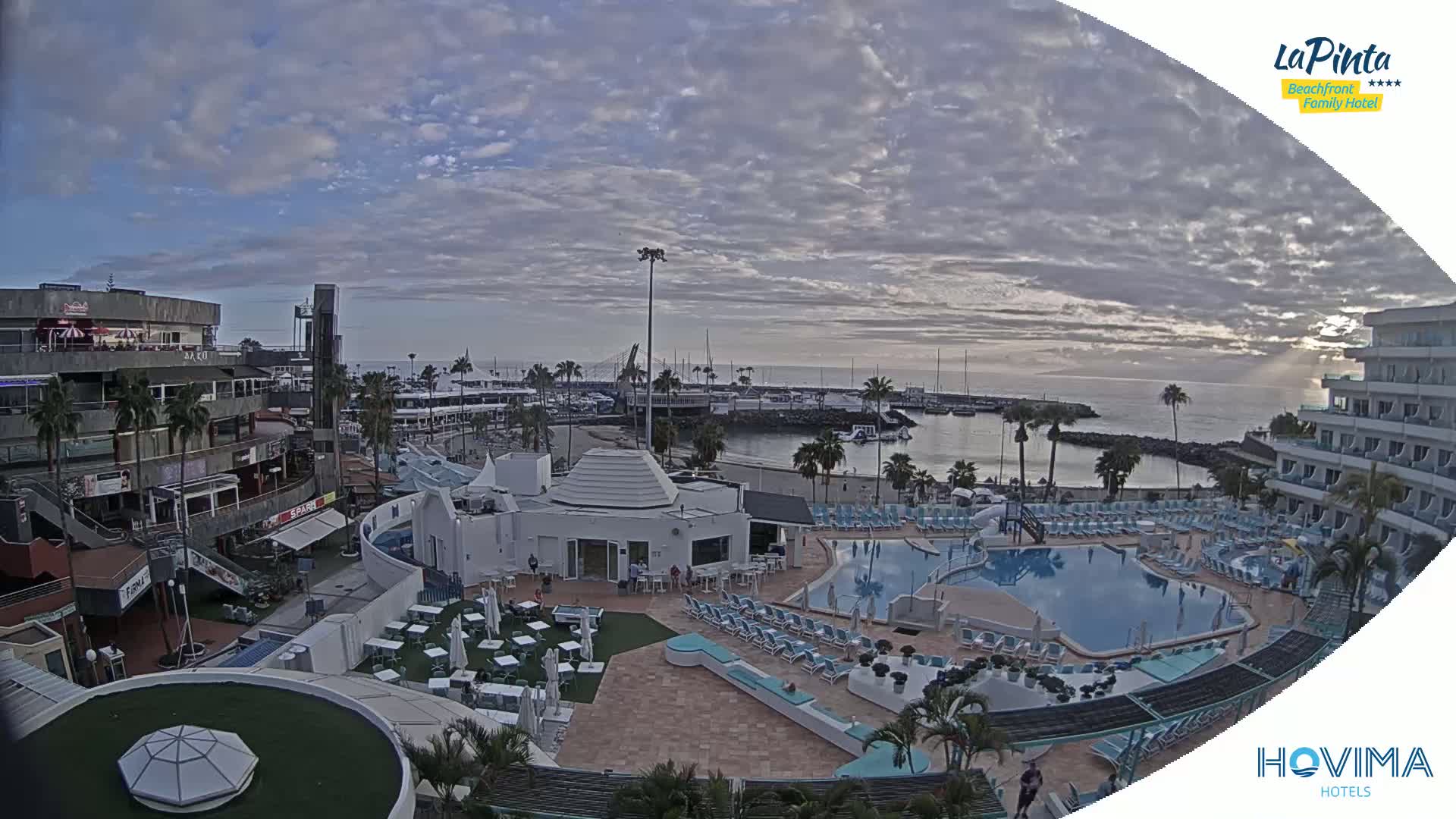 An overcast day reveals a resort area with a swimming pool and a marina, overlooking the ocean.