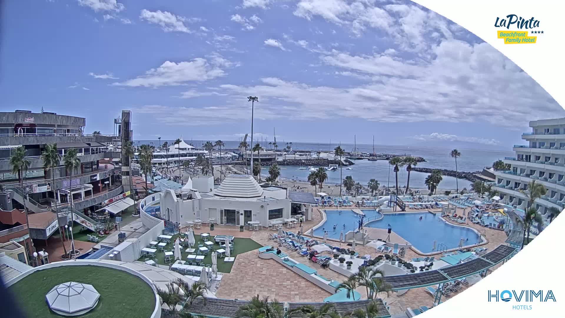 A partly sunny day shows a resort with multiple pools overlooking a marina and beach.