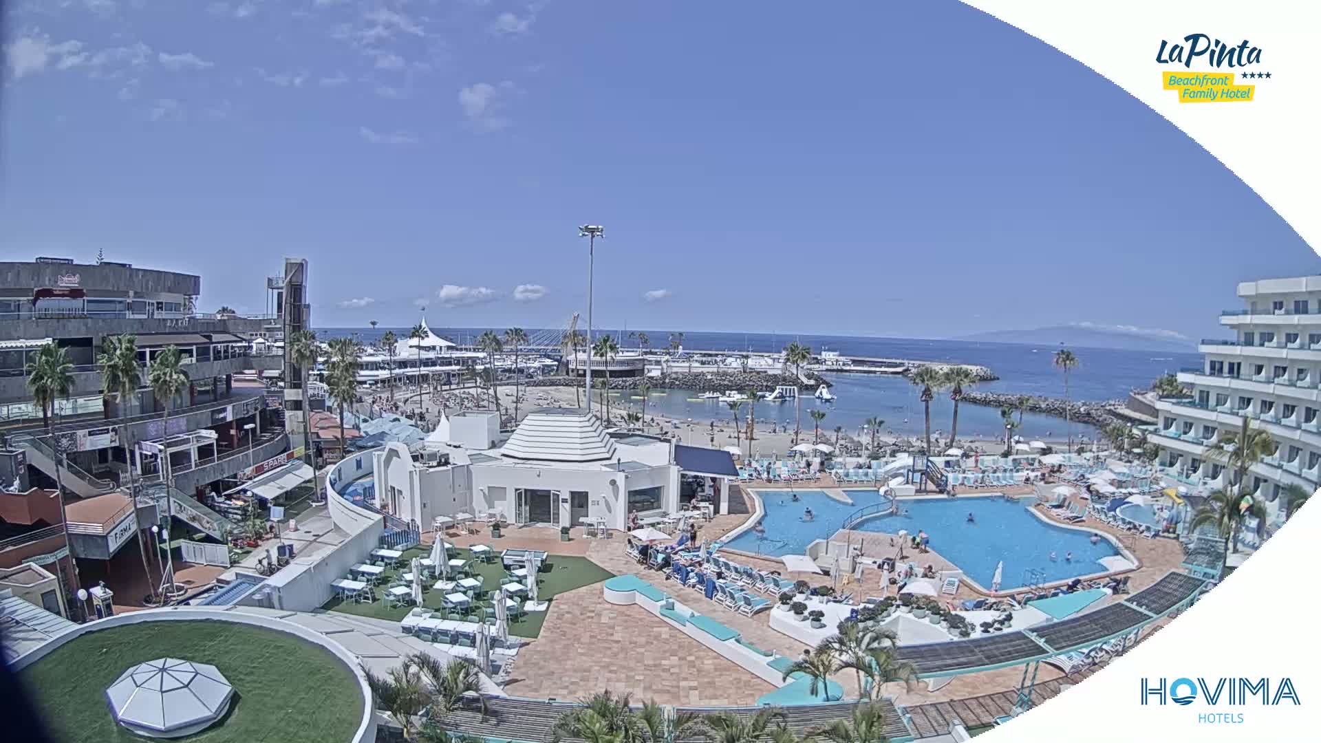 An aerial view shows a resort with a pool and beach area on a sunny day.