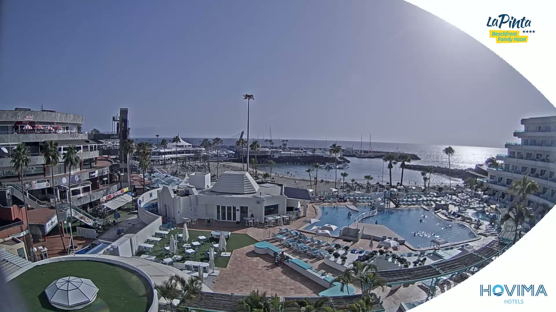 A sunny day overlooking a resort with a swimming pool, beach, and marina, under a clear blue sky.