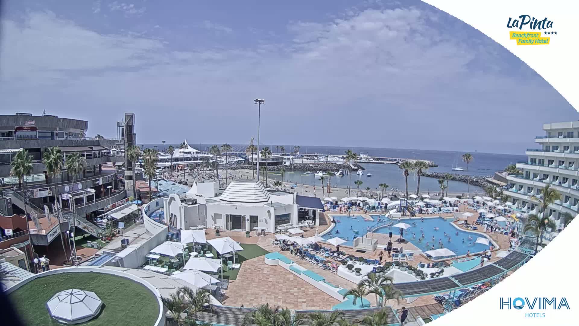 A resort pool area with a beach and marina in the background on a sunny day.