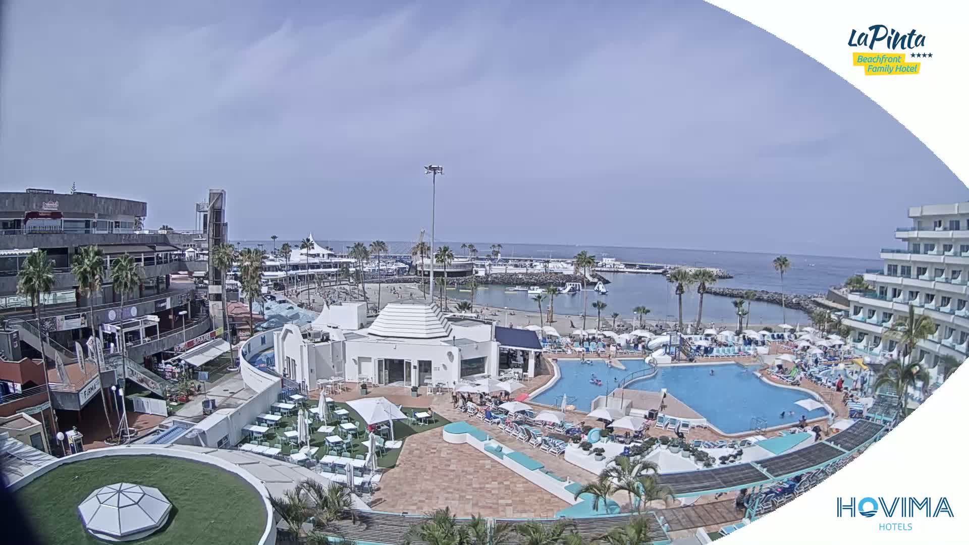 A resort pool area with a beach and calm ocean in the background on a sunny day.