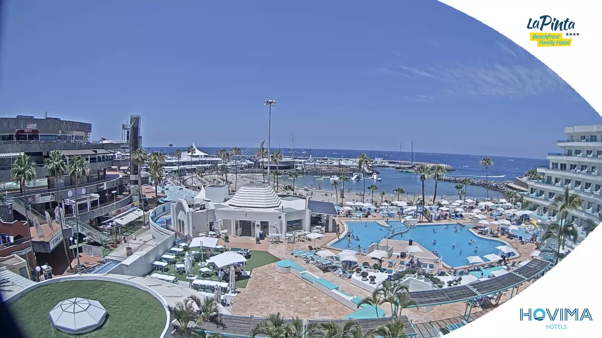A sunny day overlooking a resort with a swimming pool and beach area next to a marina and ocean.