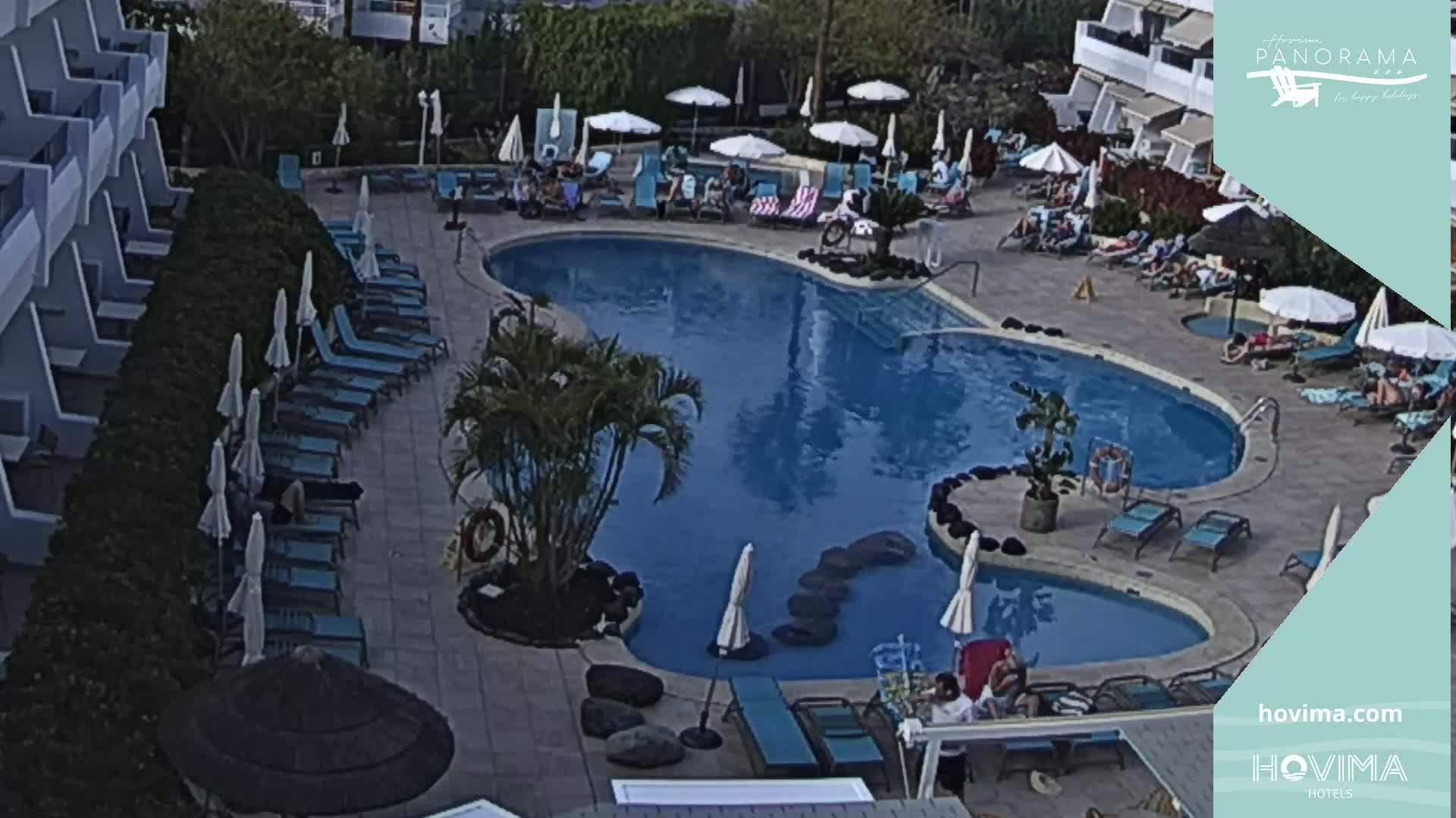 An outdoor swimming pool with surrounding lounge chairs and umbrellas at a hotel, under a partly sunny sky.