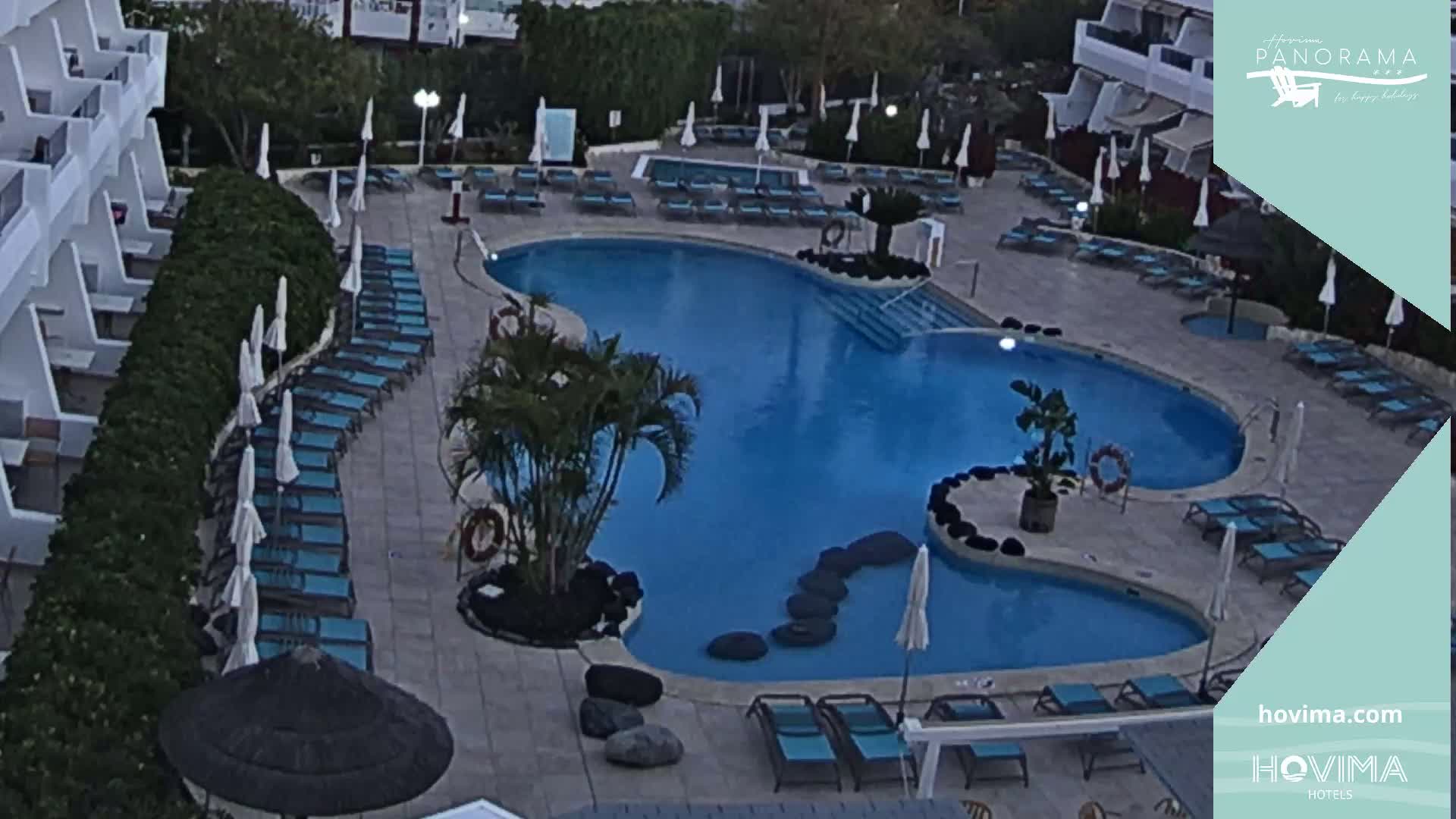An outdoor swimming pool surrounded by lounge chairs and umbrellas at dusk or dawn.