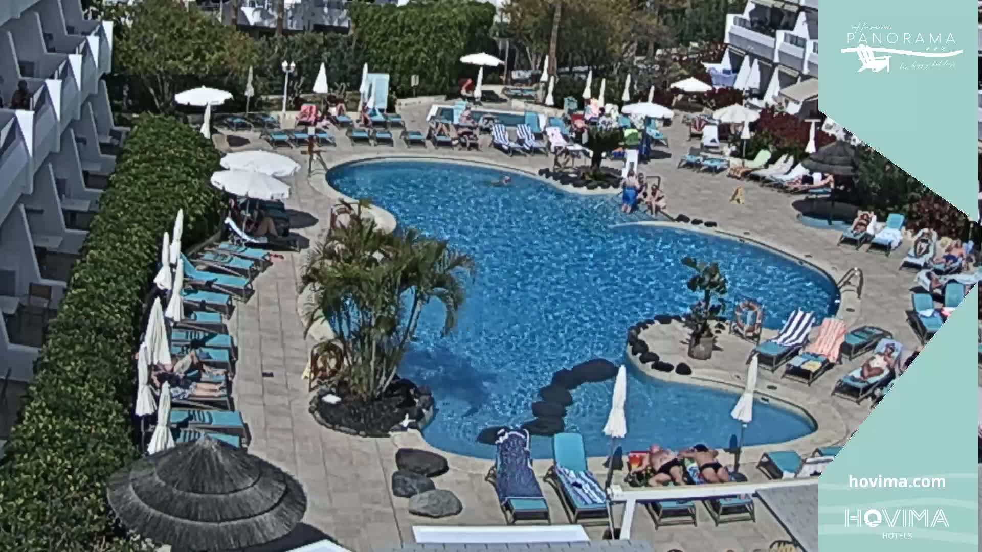 An outdoor swimming pool surrounded by lounge chairs and umbrellas under sunny skies.