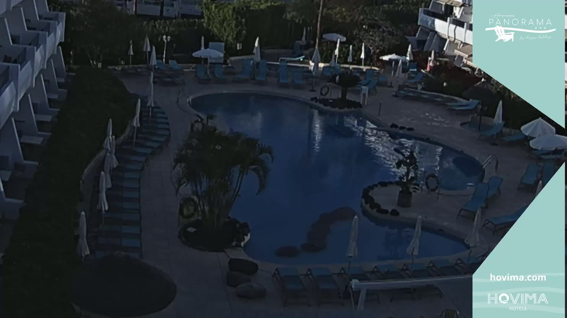 An outdoor pool area with lounge chairs and umbrellas surrounding a kidney-shaped pool at dusk or dawn.