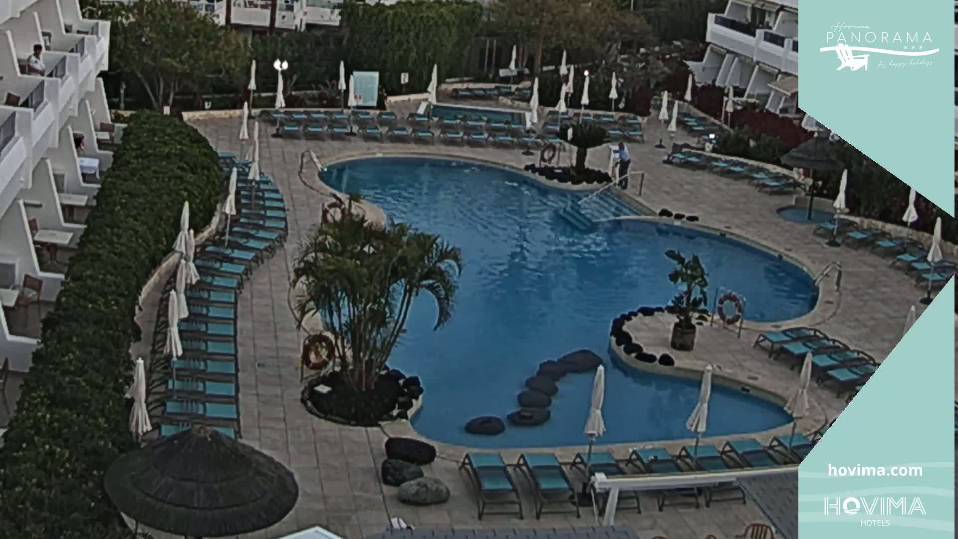 An outdoor pool with surrounding lounge chairs and umbrellas at a resort, under overcast skies.