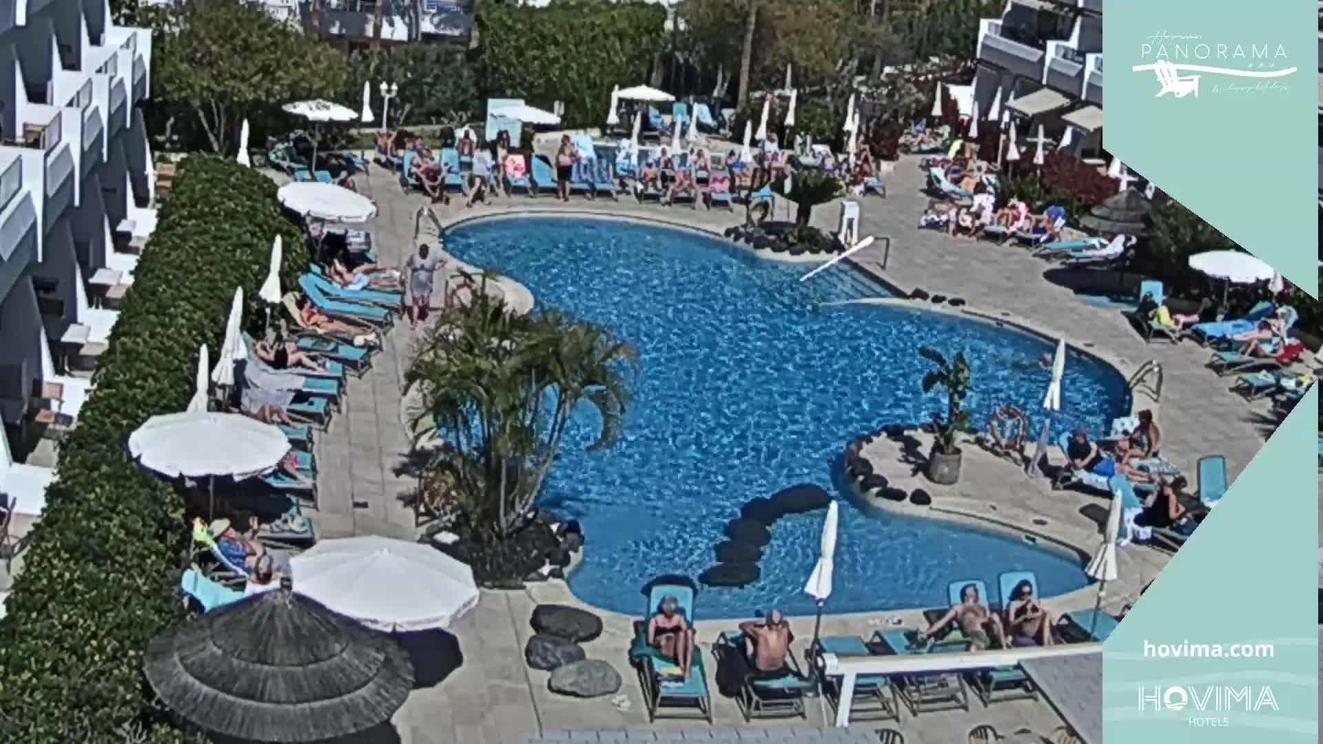 An outdoor pool area with many people sunbathing and swimming on a sunny day.
