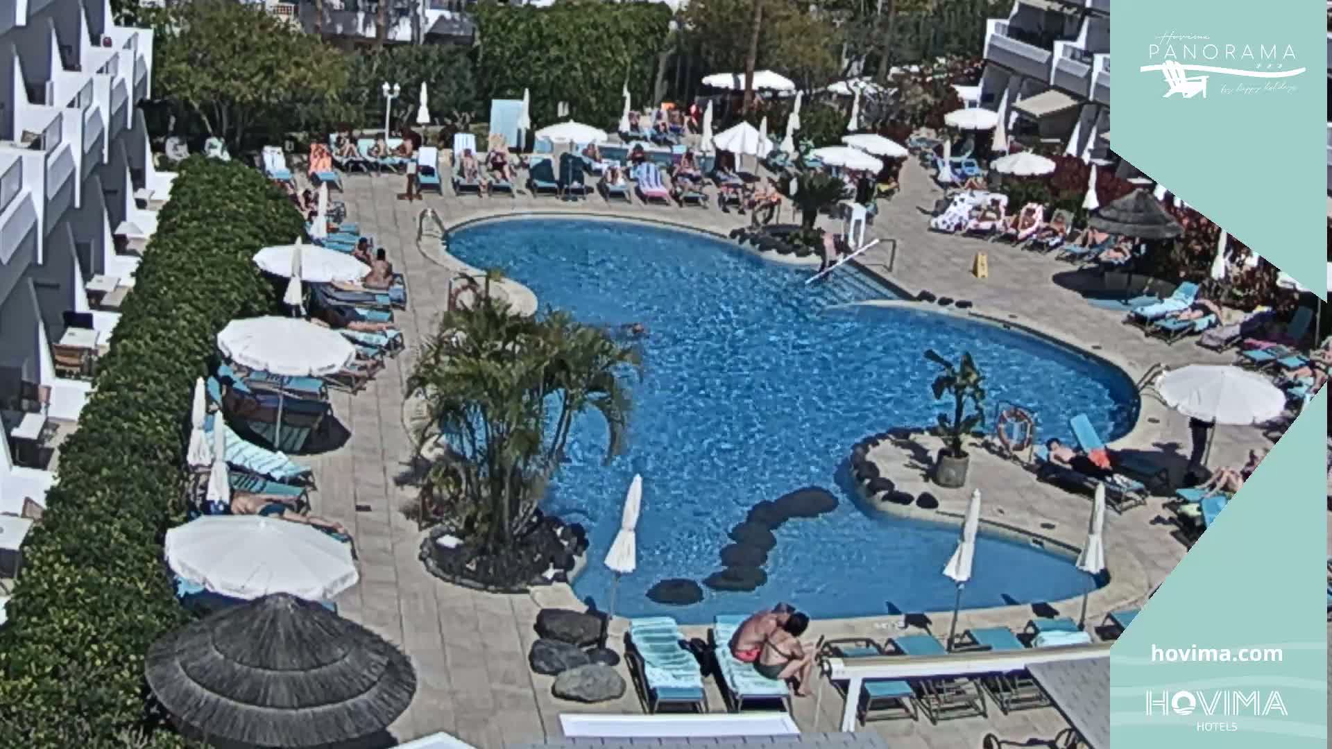 An outdoor swimming pool surrounded by lounge chairs and umbrellas under sunny skies.